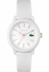 Montre en silicone blanche avec un bracelet texturé, affichant un cadran blanc, des index horaires dorés et un logo de crocodile vert. Design rond et minimaliste.