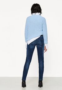 Light blue knit sweater, oversized fit, layered over a white shirt, paired with dark blue skinny jeans and black ankle boots.