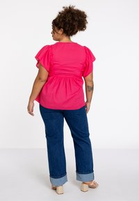 Rosa Puff-Ärmeltop mit gerafftem Detail in der Taille, kombiniert mit blauen Jeans aus Denim, die an den Säumen gerollt sind, und beigen Sandalen mit Blockabsatz.