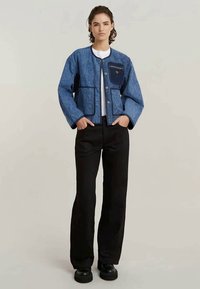 Modrá prešívaná bunda s okrúhlym krkom, tmavomodrými vreckami a čiernymi nohavicami. Obsahuje gombíky a voľný strih. Textúrovaný denimový materiál.