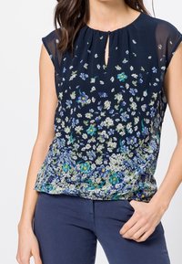 Námořnická halenka s květinovým potiskem; lehká, strukturovaná látka; kulatý výstřih s detailem v podobě klíčov hole; krátké rukávy v kapkovém stylu; nařasený pas.