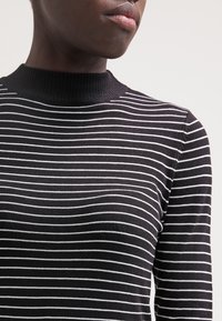 Musta-valkoraidallinen pitkähihainen paita, jossa on resorikangas ja poolokaulus. Kangas vaikuttaa pehmeältä ja sileältä. Ei näkyviä kuvioita tai yksityiskohtia.