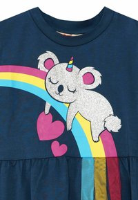 Dunkelblaues T-Shirt mit einem glitzernden weißen Koala mit einem Einhornhorn, der auf einem bunten Regenbogen mit rosa Herzakzenten ausruht.