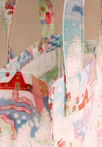 Tkaninska vrečka z barvitimi vzorci hiš, dreves in snega. Mehka tkanina, trdno šivanje in kratki ročaji za prenašanje.