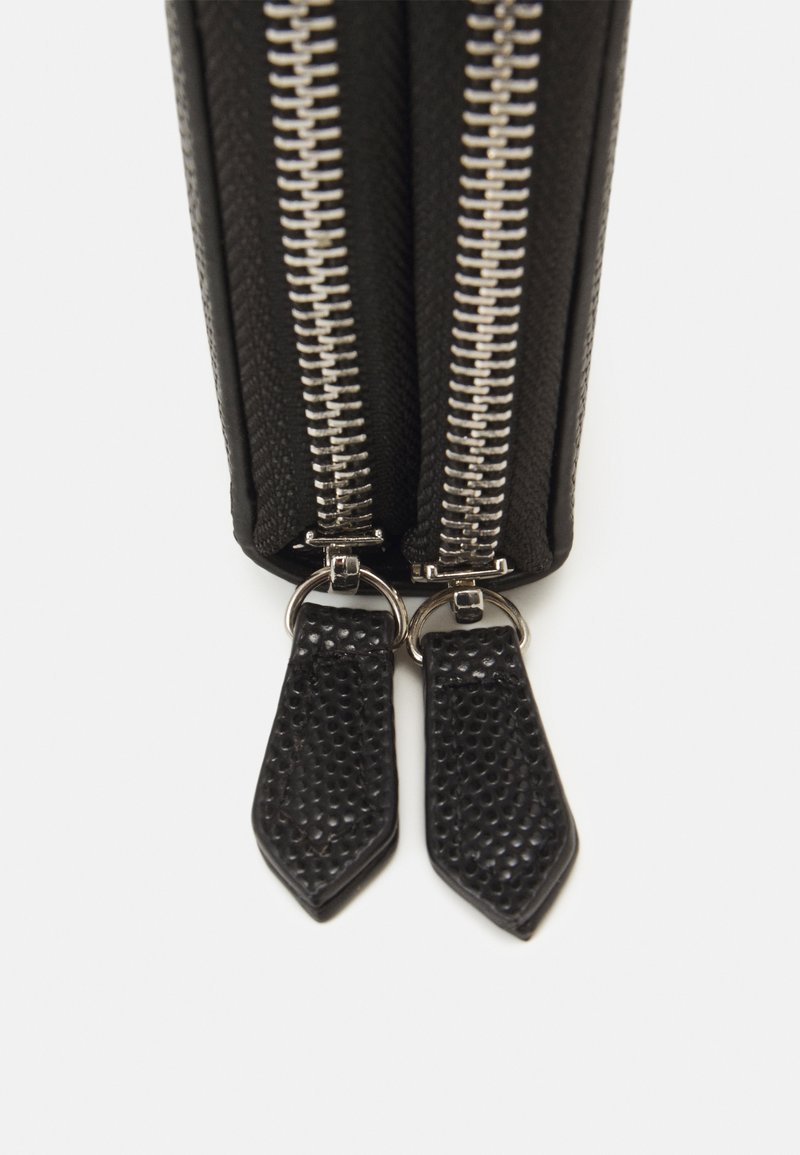 Schwarze Tasche mit doppelt silbernen Reißverschlüssen, ausgestattet mit strukturierten Reißverschlusszügen aus schwarzem Leder. Das Material wirkt robust und hat ein strukturiertes Design.