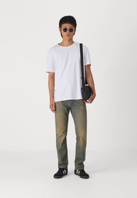 Hvit t-skjorte, falmede blå jeans, svarte sneakers med hvite striper, runde solbriller. Svart crossover-veske med stropp.