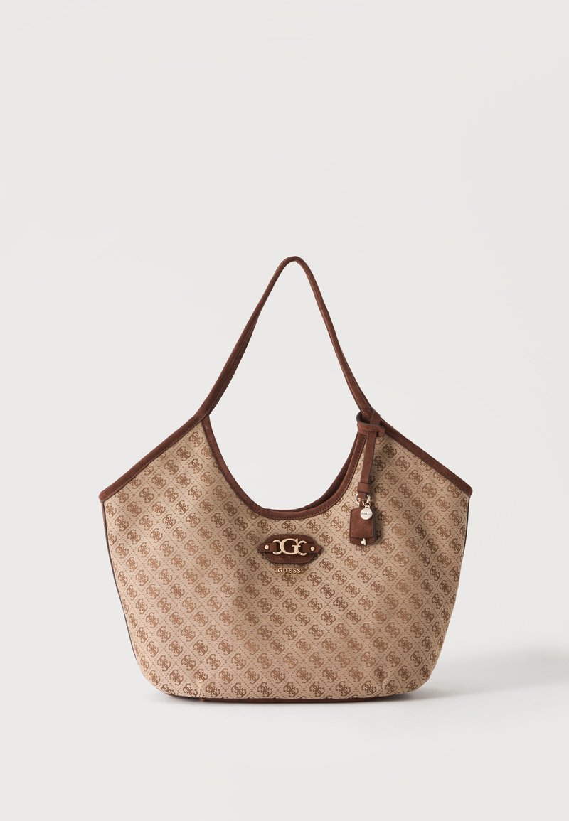 Sac cabas Guess beige et marron à motifs avec une bandoulière unique, plaque logo et petite étiquette suspendue sur un fond neutre.