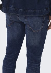 Jeans din denim de culoare albastră închisă, cu un design ajustat, buzunare din spate vizibile și detalii ușoare de decolorare pe țesătură. Finisaj curat cu accente de cusătură subtile.