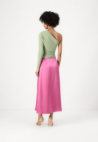 Asymmetrical top in light green with one long sleeve, paired with a pink maxi skirt. Smooth texture, fitted waist, and flat sandals.