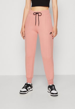 Rožinės sportinės kelnės su raštuotu juosmeniu ir reguliuojamu raišteliu, turinčios šonines kišenes ir juodą „Nike“ logotipą virš šlaunies.