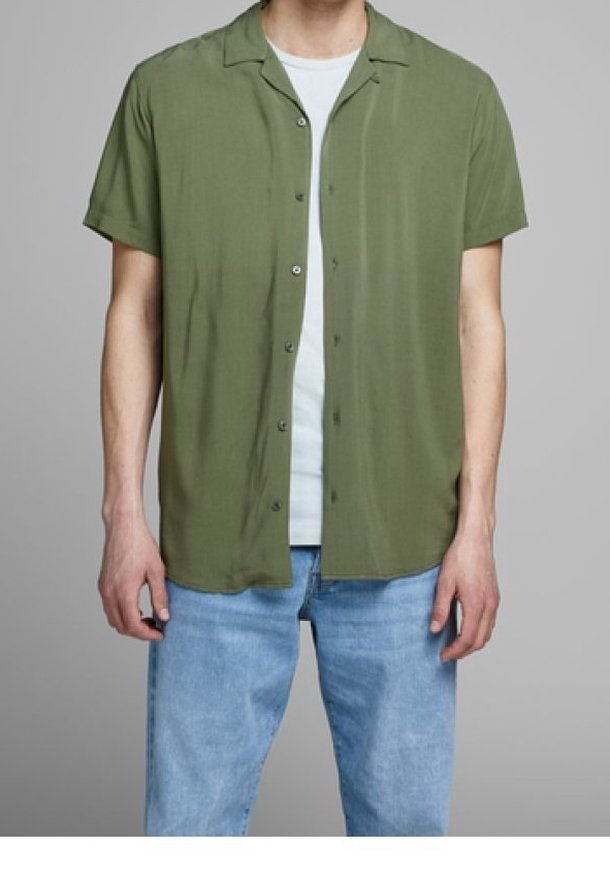 Korte mouwen, knoopshirt in olijfgroen, gemaakt van lichte stof. G gedragen over een wit T-shirt, gecombineerd met lichtblauwe denim jeans.