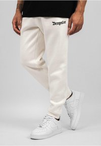 Hvide sweatpants med sort "Dropsize" bogstavprint, børstet tekstur, elastiske manchetter, parret med hvide sneakers med en glat overflade.