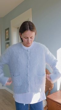 Jasnoniebieski, puszysty kardigan z miękkiego materiału, zapinany na guziki, z dwiema przednimi kieszeniami i długimi rękawami.