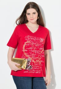 Camiseta de algodón roja con escote en V, que presenta un gráfico floral y un diseño de texto a mano. Combinada con un bolso de mano metálico dorado.