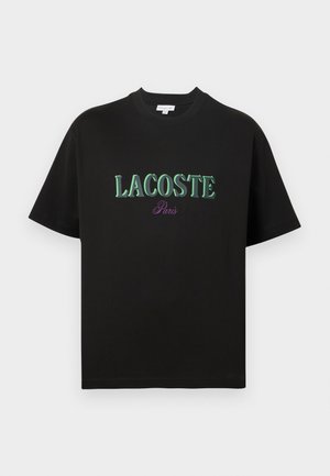 T-shirt preta de algodão com mangas curtas, com texto verde "LACOSTE" e "Paris" em roxo abaixo. Design simples, decote redondo padrão.