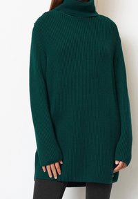 Grüner gerippter Strickrollkragenpullover mit langen Ärmeln, seitlichen Schlitzen und lockerer Passform. Strukturierter Stoff mit dicker, gemütlicher Optik.