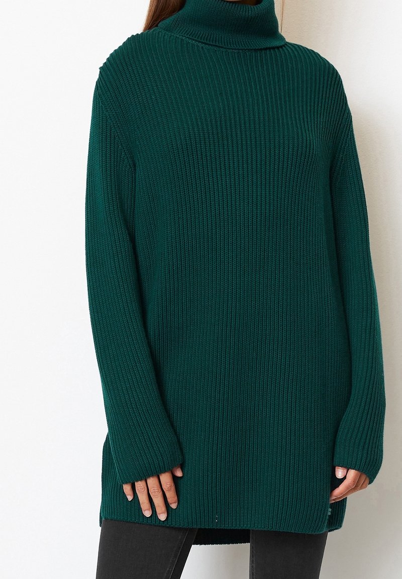 Grüner gerippter Strickrollkragenpullover mit langen Ärmeln, seitlichen Schlitzen und lockerer Passform. Strukturierter Stoff mit dicker, gemütlicher Optik.