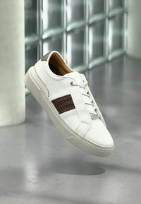 Weißer Sneaker aus Leder mit braunem gewebtem Akzent, flachem Schnürdesign und glatter Gummisohle. Minimalistisch mit schlankem Profil.