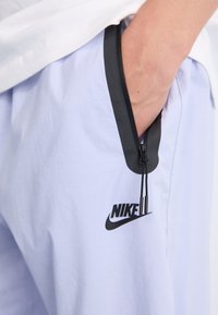 Világoslila rövidnadrág fekete cipzáros zsebbel, Nike logóval. Simázs felület és minimalista dizájn fekete részletekkel.
