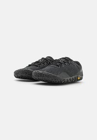 Black low-profile shoes with a textured mesh upper, minimalistic design, and rugged rubber outsole featuring a distinctive tread pattern.
