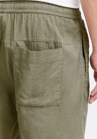 Pantaloni scurți verde măsliniu din material texturat, cu croială lejeră, prevăzuți cu un buzunar în spate și talie elastică.