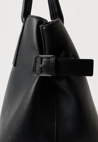 Crna torba od teksturirane kože sa srebrnom pravokutnom kopčom i čvrstim ručkama na svijetloj jednobojnoj pozadini.