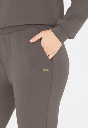 Graue, lässige Jogginghosen mit einer glatten Textur, ausgestattet mit Seitentaschen und einem kleinen goldfarbenen Markenakzent am Bein.