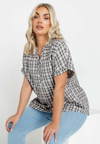 Camicia a maniche corte a quadri grigia e nera con bottoni frontali, vestibilità rilassata e tessuto morbido e leggero. Jeans in denim blu chiaro la completano.