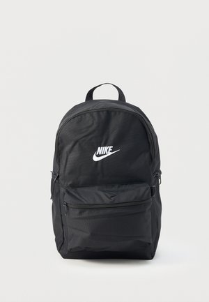 Czarny plecak Nike z białym logo, przednią kieszenią na zamek, górnym uchwytem i paskami na ramiona na jednolitym jasnym tle.