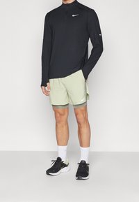 Schwarzes Nike Langarmshirt mit Reißverschluss, mintgrüne Shorts und schwarze Nike-Schuhe mit weißen Akzenten. Weiße Socken sind sichtbar.