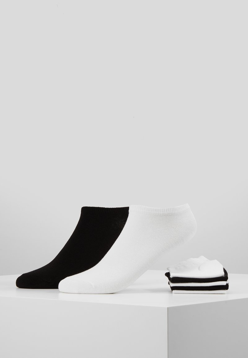 Schwarz-weiße Knöchelsocken. Die schwarze Socke hat eine glatte Textur; die weiße Socke hat gerippte Akzente. Drei weitere gestreifte Socken sind daneben gestapelt.