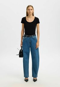 Sort scoop-neck t-shirt kombineret med højtaljede, løse blå jeans. Modellen holder en lille sort taske og har sorte spidse højhælede sko på.