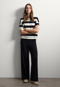 Top a righe bianco e nero, maniche corte; pantaloni neri a gamba larga; scarpe in tono neutro. Design minimalista con una texture di tessuto liscia.