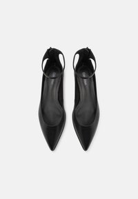 Flats en cuir noir à bout pointu avec des brides autour de la cheville et des fermetures éclair arrière, arborant un logo Calvin Klein sur les semelles intérieures.