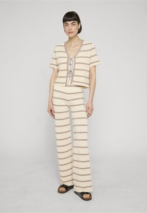Woman standing wearing beige and taupe horizontal striped short-sleeve top with front ties and matching wide-leg pants with black sandals.