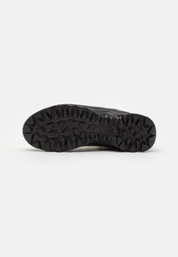 Black sports shoe featuring a textured rubber outsole with a multi-directional grip pattern for traction and stability.
