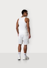 Weißes Tanktop mit einer figurschmeichelnden Passform, kombiniert mit knielangen weißen Shorts; beide besitzen eine glatte Textur und einen minimalistischen Stil.
