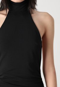 Melnas bezpiešu topiņš ar augstu kakla dizainu, izgatavots no gludas auduma, ar pieguļošu struktūru un minimāliem šuvju detalizējumiem.