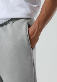 Lichtgrijze sweatpants met een gladde textuur, zijzakken en een elastische tailleband. De stof lijkt zacht en ademend.