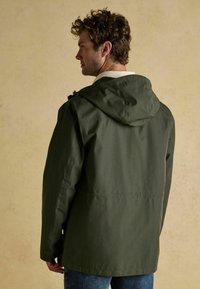 Alyvuogių spalvos džinsinis švarkas su suplonu audiniu, be detalių nugaroje ir su reguliuojamu raišteliu apykaklėje. Kasdienis siluetas su ilgomis rankovėmis.