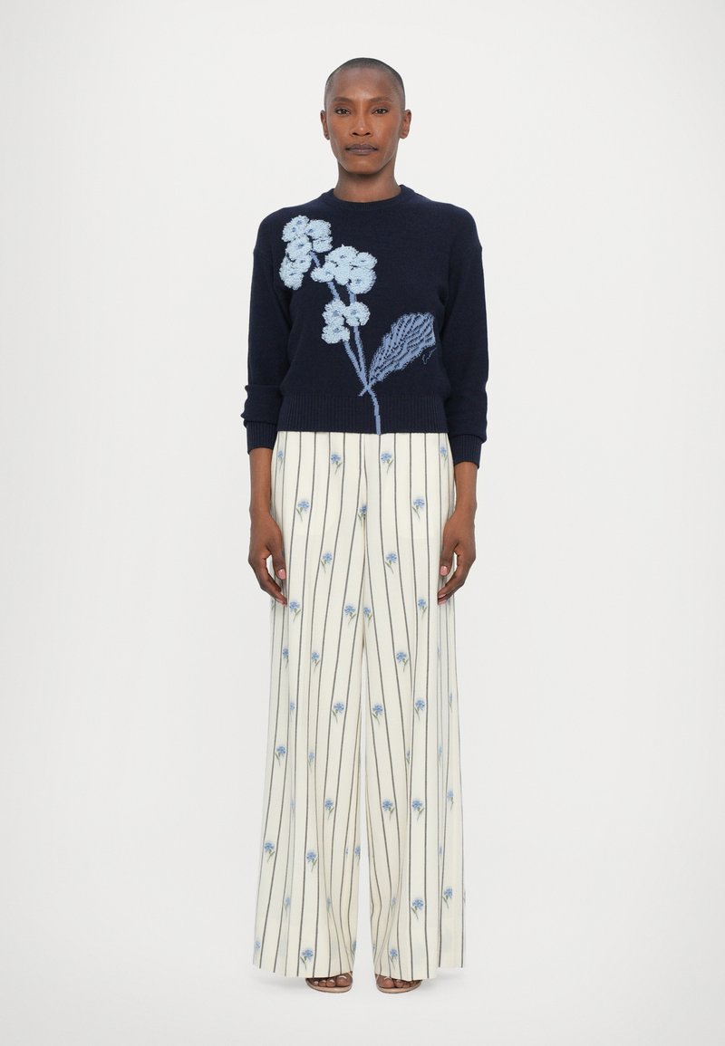 Navy knitted sweater with short sleeves featuring blue floral embroidery at the shoulder, paired with wide-leg cream pants with blue floral patterns.