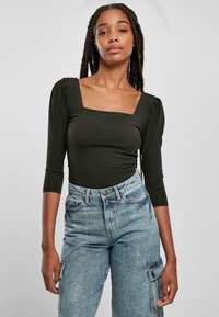 Svart langermet bodysuit med firkantet utringning, laget av elastisk stoff. Kombinert med lyseblå høytidte denimjeans med sidelommer.