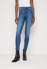Jeans ajustados en denim de lavado medio, con una silueta ceñida, cintura de altura media y un sutil detalle de costura. Combinados con botas negras hasta el tobillo.