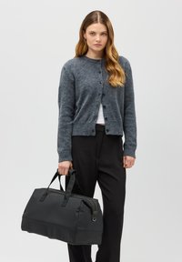 Šedý vlněný cardigan s kulatým výstřihem a knoflíky, kombinovaný s černými kalhotami a černou matnou taškou typu duffle se dvěma rukojeťmi.