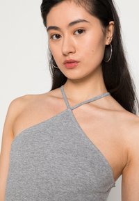 Top halter cinza feito de tecido canelado, apresentando um design de alças cruzadas e uma gola assimétrica, abraçando suavemente os contornos do corpo.