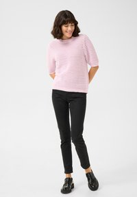 Hele roosa koonuseline sviiter lühikeste varrukatega, millel on tekstuuriline muster. Sobitatud mustade kitsaste pükste ja mustade loafer'itega.