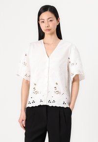 White button-up blouse with short, flared sleeves, featuring floral embroidery and open cut-out details at the hem. Textured fabric.