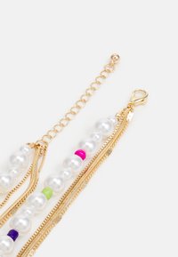 Acessório de corrente dourada com pérolas brancas brilhantes alternadas e contas coloridas em rosa, verde e roxo. Inclui um fecho tipo lagosta.