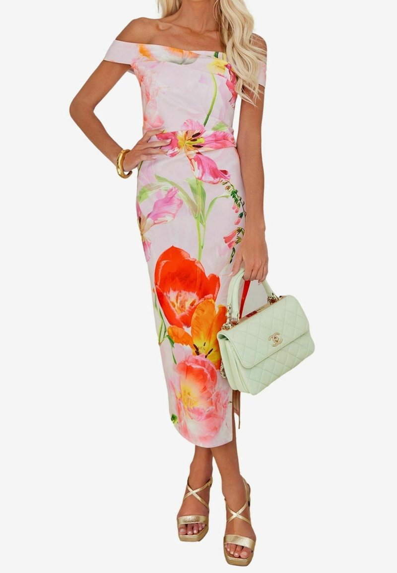 Femme portant une robe florale rose à épaules dénudées, tenant un sac à main matelassé vert clair et des sandales dorées à talons hauts.
