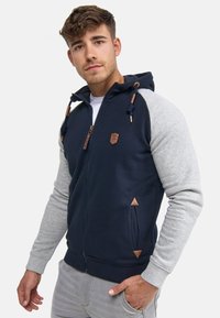 Navy and gray zip-up hoodie made from cotton blend, featuring a hood, leather accents, and triangular details on pockets.